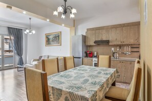 Un coin repas comprenant une table, des chaises, un lustre, une cuisine avec des meubles en bois et un tableau accroché au mur.
