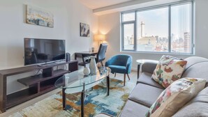 Een moderne woonkamer met een flatscreen televisie, een glazen salontafel, een bank en een groot raam met uitzicht op de stad.