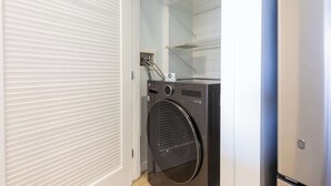 Een wasserette met een voorlader wasmachine en droger, een metalen schapkas en een witte deur.