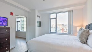 Een moderne hotelkamer met een groot bed, een televisie, een dressoir en uitzicht op de stad.