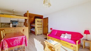 Un espace de vie compact comprenant une table à manger, un canapé, un petit meuble en bois et une kitchenette.