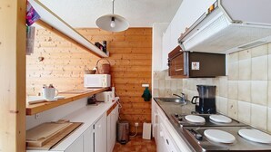 Une cuisine compacte avec des murs en bois, un four à micro-ondes, une bouilloire, un évier et une cuisinière.