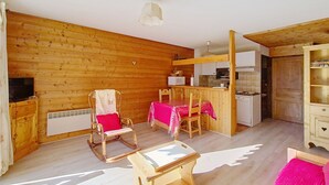 Un intérieur de chalet chaleureux, avec un revêtement en bois, un coin repas comprenant une table et des chaises, un coin cuisine et un téléviseur.