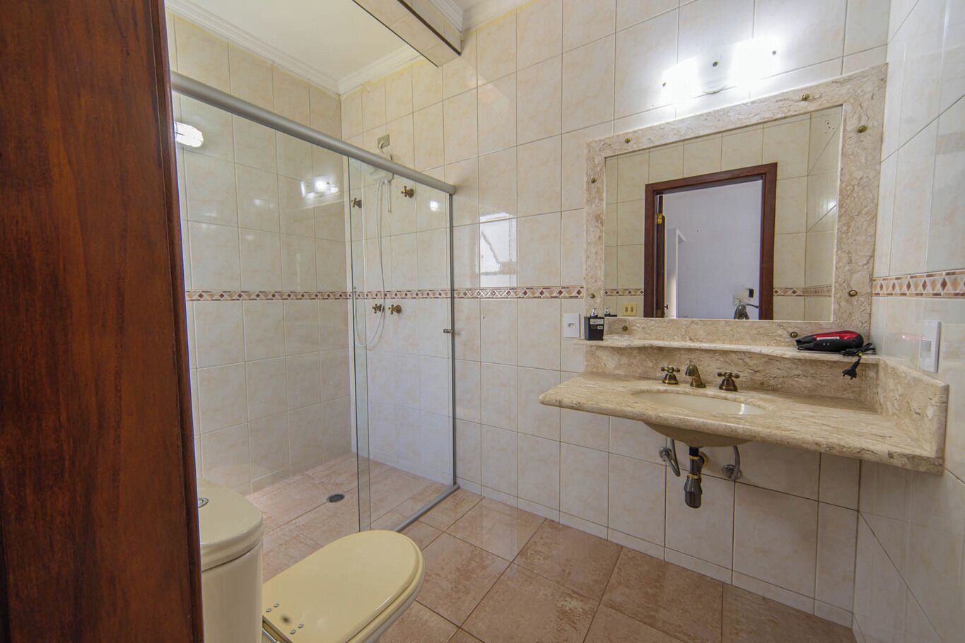 Ein Badezimmer mit Duschkabine aus Glas, Toilette, Waschbecken mit Spiegel und Marmorplatte.