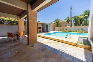 A covered patio area with a pool, outdoor seating, and a brick column. - Casa c Piscina e Churrasqueira em Condom nio (Guarujá)