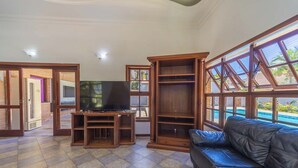 A spacious living room with a flat-screen TV, wooden entertainment unit, and a leather sofa. - Casa c Piscina e Churrasqueira em Condom nio (Guarujá)