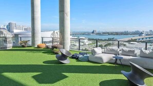 Eine Dachterrasse mit grüner Kunstrasen, weißen Sofas und Blick auf Stadt und Wasser.