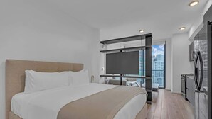 Ein modernes Hotelzimmer mit einem großen Bett, einem Flachbildfernseher, einer kleinen Küchenzeile und Blick auf die Stadt.
