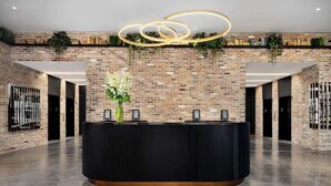 Un espace d’accueil avec un mur en briques, un comptoir d’accueil noir et un luminaire circulaire moderne.