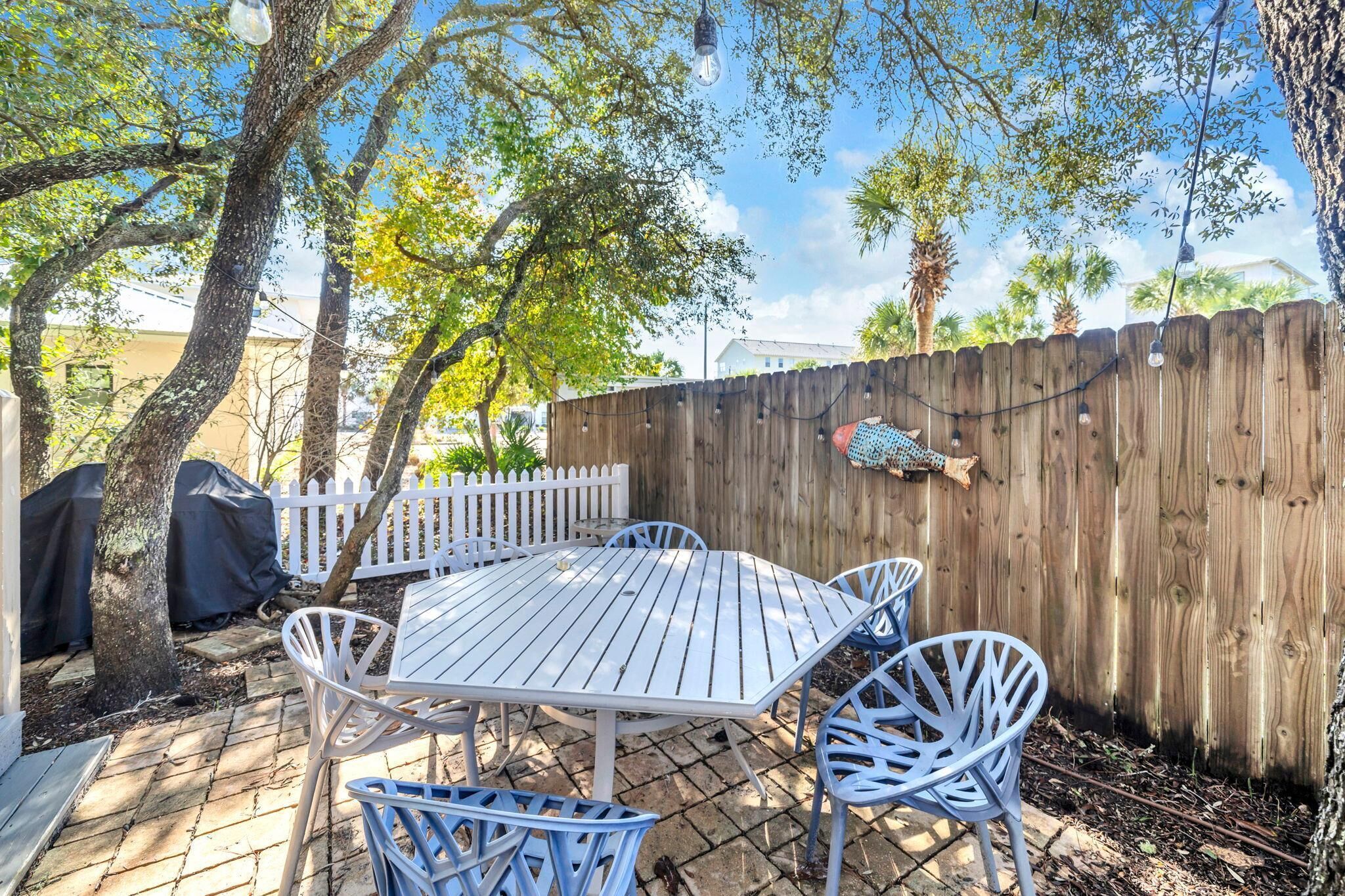 An outdoor patio with a white metal table and chairs, a wooden fence, and trees.
