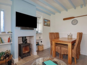 A living room with a fireplace, a television mounted on the wall, a dining table with chairs, and a clock on the wall. - Puffin Cottage (Tintagel)