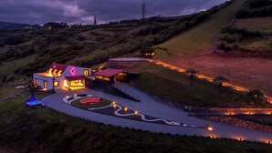 Et moderne hus med swimmingpool, omgivet af bakker og en oplyst indkørsel.