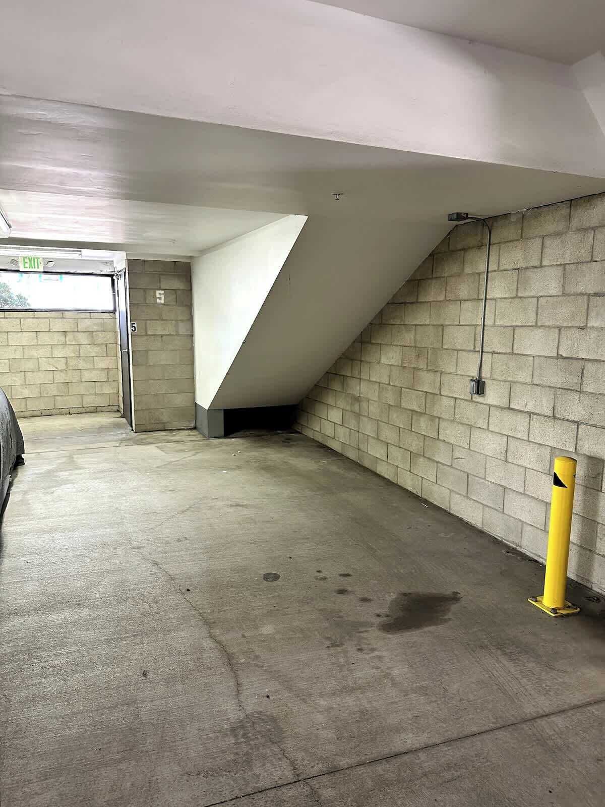 A parking garage with concrete walls, a sloped ceiling, and a yellow bollard.