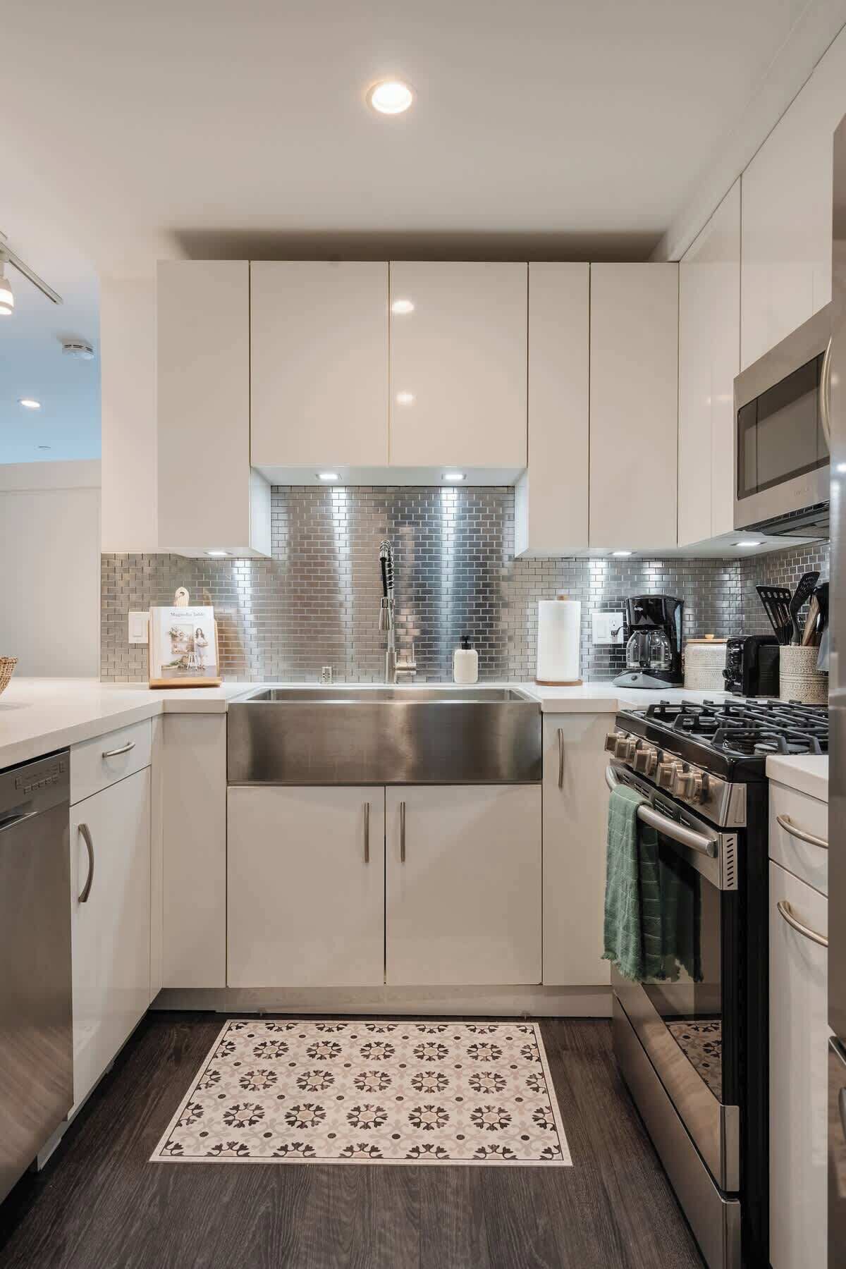 Una cucina moderna con elettrodomestici in acciaio inossidabile, zoccolo paraschizzi rivestito in piastrelle e mobili chiari.