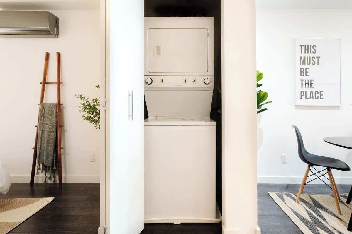 A compact laundry room with a washing machine and dryer, a wooden ladder, and a small plant.