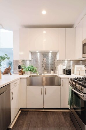 A modern kitchen with white cabinets, a stainless steel sink, and a built-in stove. - Elegant Little Italy Hideaway w/ Sky Deck & Views (San Diego)