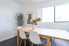 A modern dining area with a wooden table and white chairs, a potted plant, and a framed picture on the wall. - Elegant Little Italy Hideaway w/ Sky Deck & Views (San Diego)
