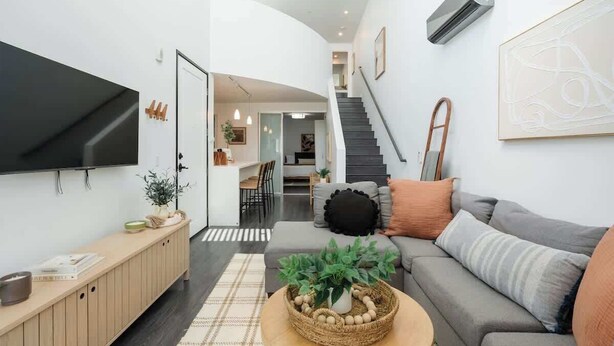Uma sala de estar moderna com televisão de tela plana, um sofá, uma mesa de centro com uma planta e uma escada que leva a outro andar.