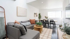 Uma sala de estar moderna com um sofá cinzento, uma mesa de centro de madeira e uma área de jantar com uma mesa e cadeiras.