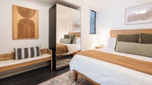 A modern hotel room with a large bed, a sofa, a mirror, and artwork on the walls. - Modern Central Gem w/ Patio | Steps to All! (San Diego)