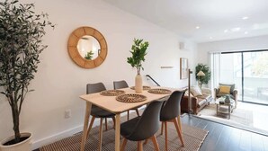 A modern dining area with a wooden table, black chairs, and a woven mirror on the wall. - Modern Central Gem w/ Patio | Steps to All! (San Diego)