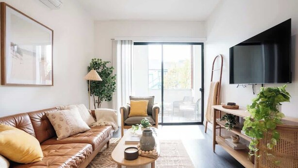 A modern living room with a leather sofa, a coffee table, a TV, and a sliding glass door leading to an outdoor area. - Modern Central Gem w/ Patio | Steps to All! (San Diego)