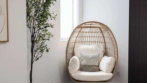 Una silla de mimbre con cojines en una habitación con un ventanal grande y una planta.