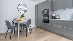 A modern kitchen with grey cabinets, a marble countertop, and a dining area with a round table and chairs. - Chic 1BR Close to Tower & Thames (London)