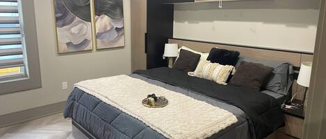 A modern bedroom with a bed, bedside tables, a nightstand, a wall-mounted shelf with plants, and abstract wall art.