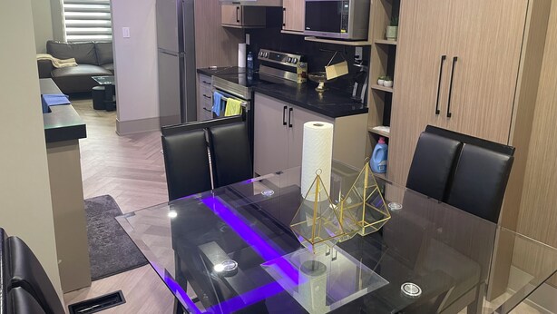Una cocina moderna con armarios de madera, encimera negra y mesa de comedor de vidrio con sillas.