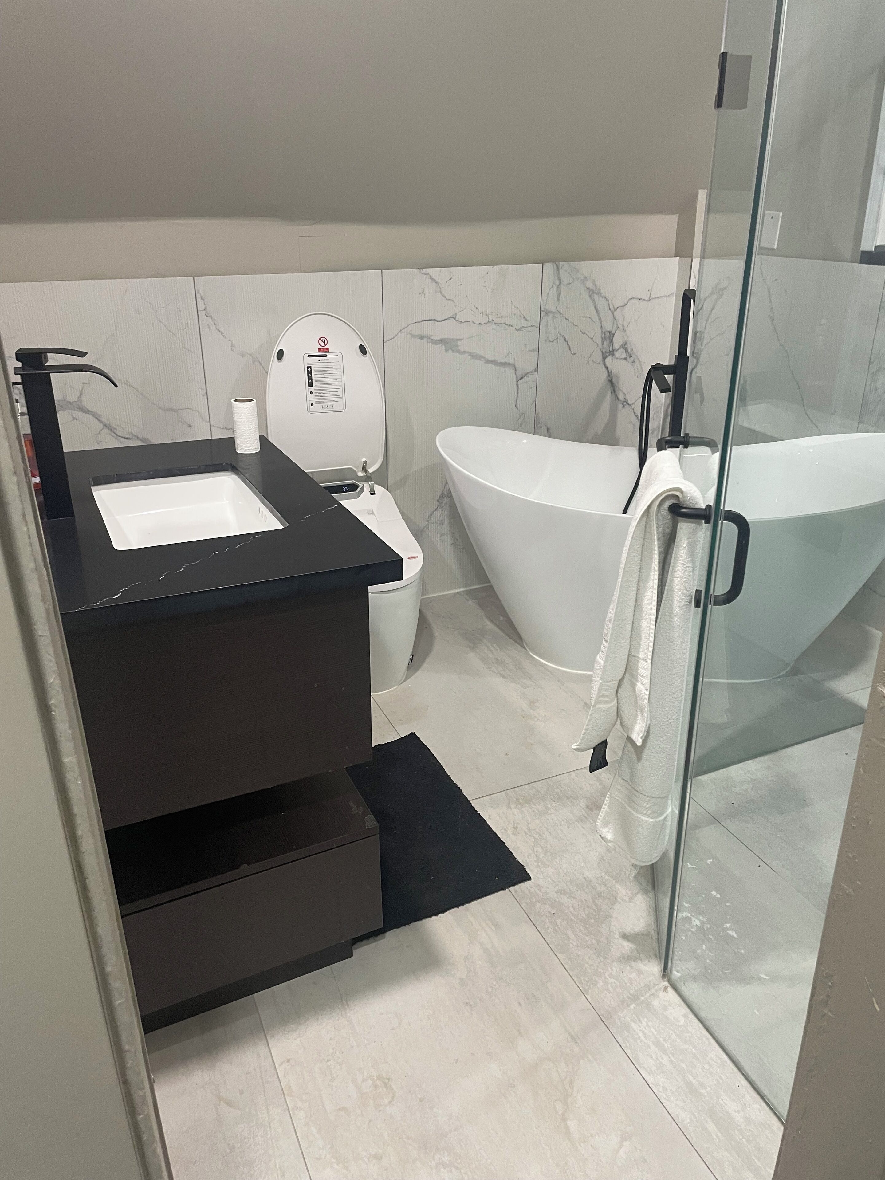 A modern bathroom with a black sink, white toilet, and a freestanding bathtub.