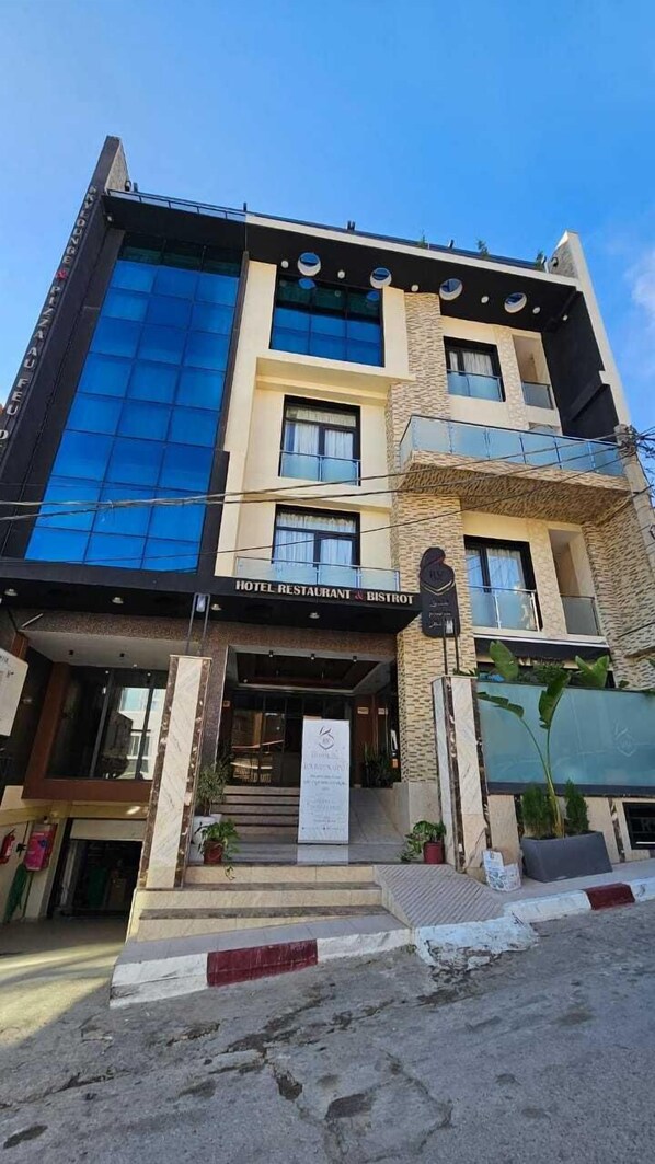 A hotel with a modern facade, featuring a prominent glass section and a sign reading "HOTEL RESTAURANT & BISTROT".