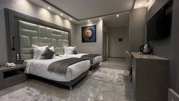 A modern hotel room with two beds, a large padded headboard, a flat-screen TV, and a painting on the wall. - RV Hotel - Dely Brahim (Algiers)