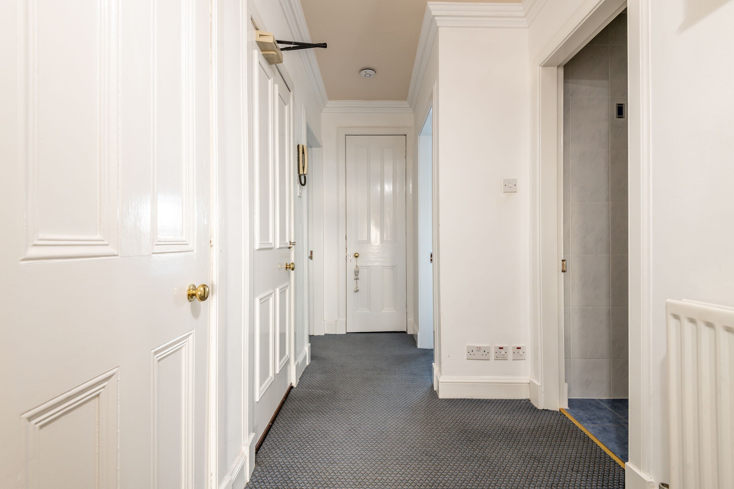 A hallway with white doors, a patterned carpet, and a radiator on the right wall.