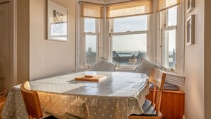 Ein Eckzimmer mit Erkerfenster, einem gerahmten Bild an der Wand und einem Tisch mit Stühlen.