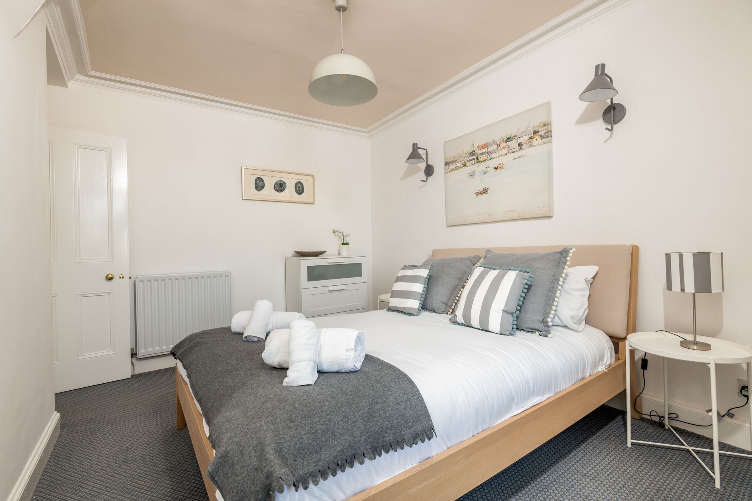 A bedroom with a bed, bedside table, lamp, and artwork on the wall.