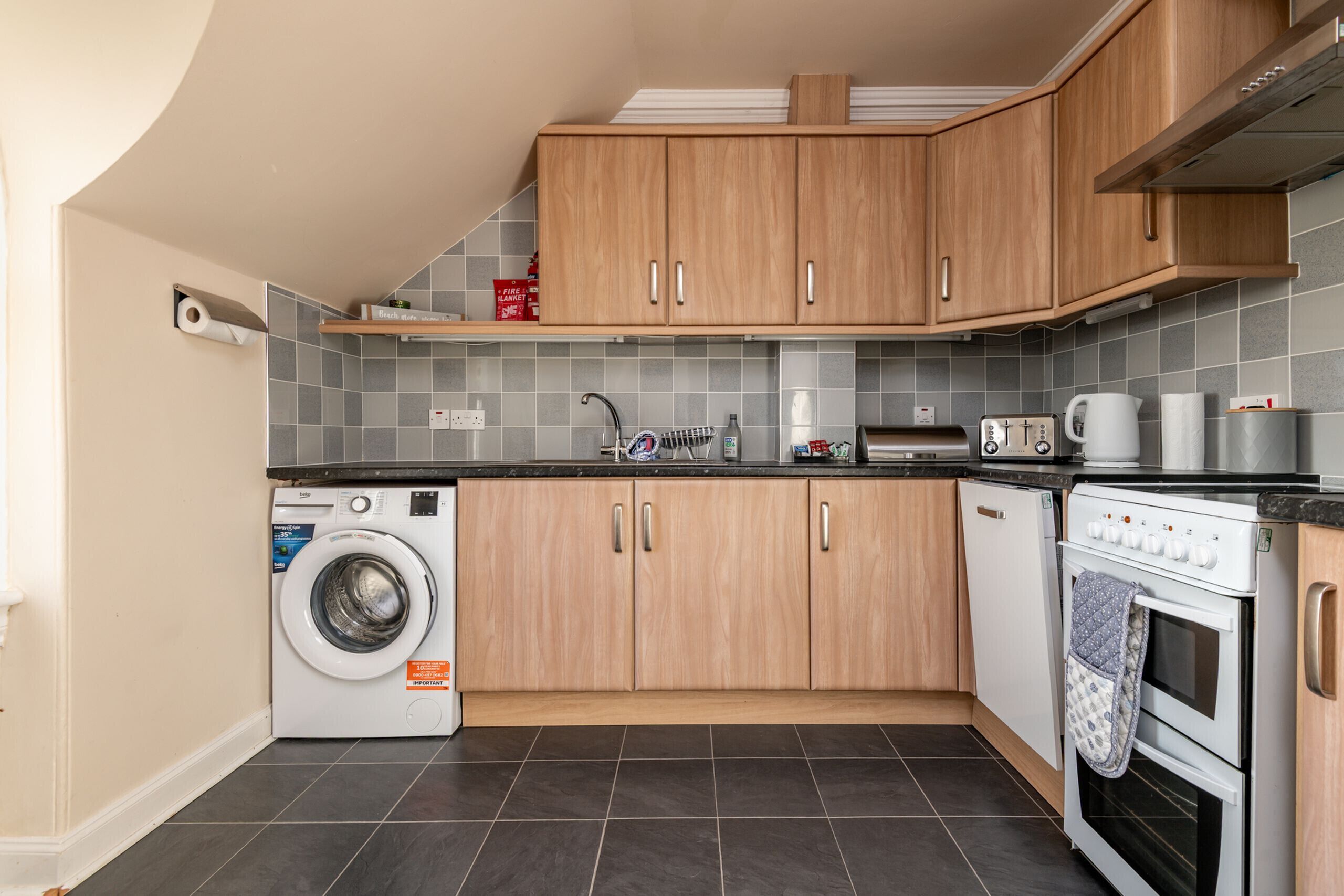 A compact kitchen with wooden cabinets, a washing machine, a microwave, and a stove.