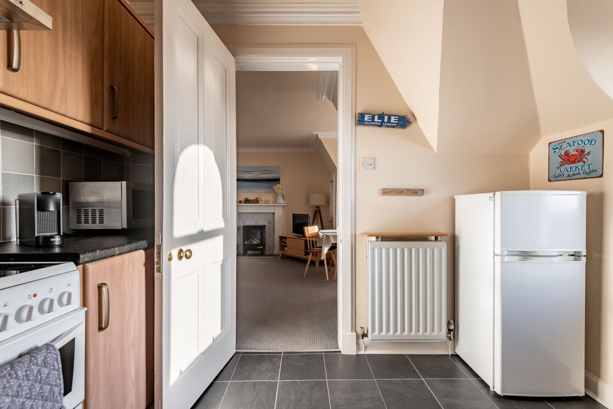 A kitchen with wooden cabinets, a white refrigerator, and a microwave. There is a sign on the wall that reads "ELIE SEAFOOD MARKET."