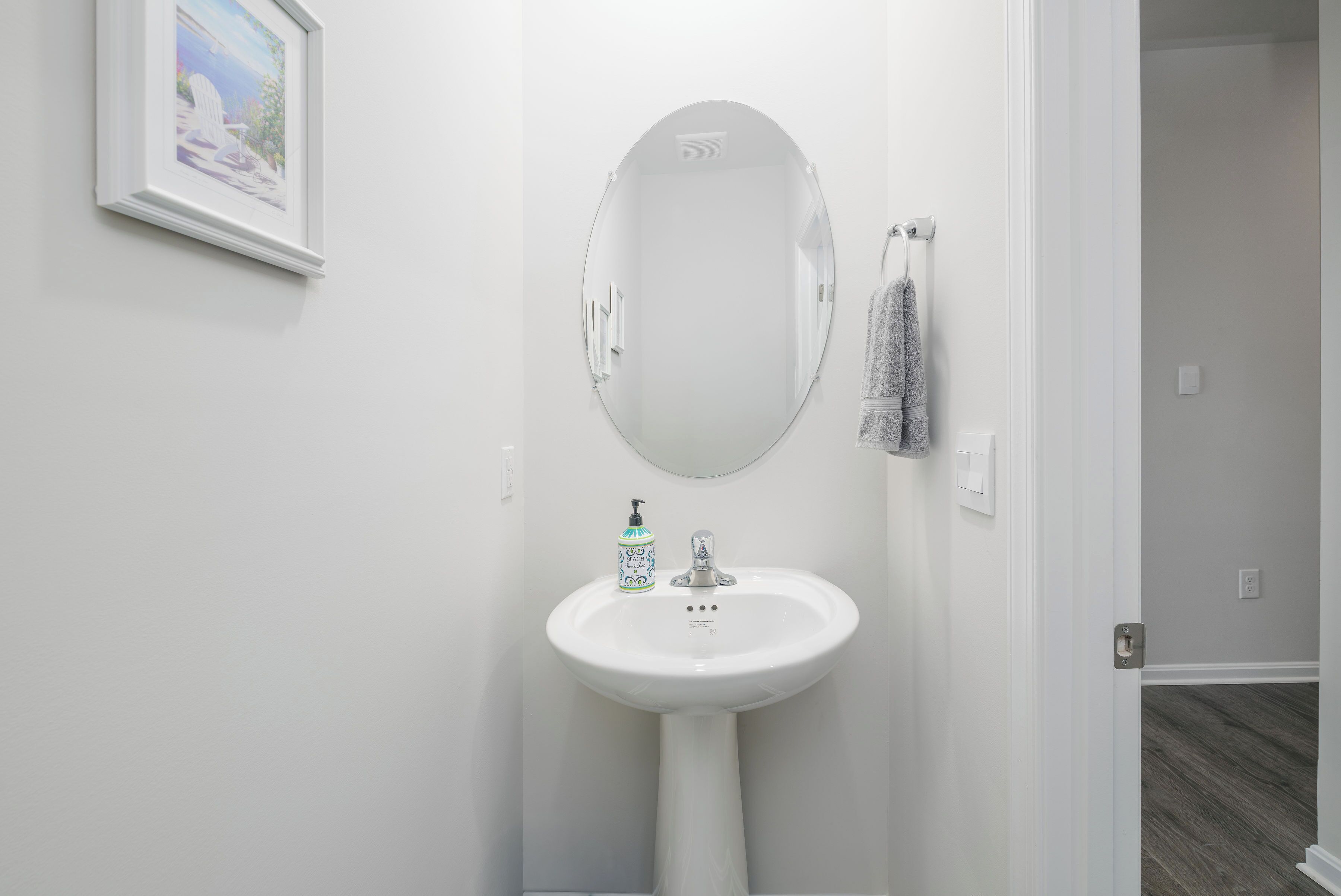 Une salle de bain avec un lavabo blanc, un miroir et un tableau encadré au mur.