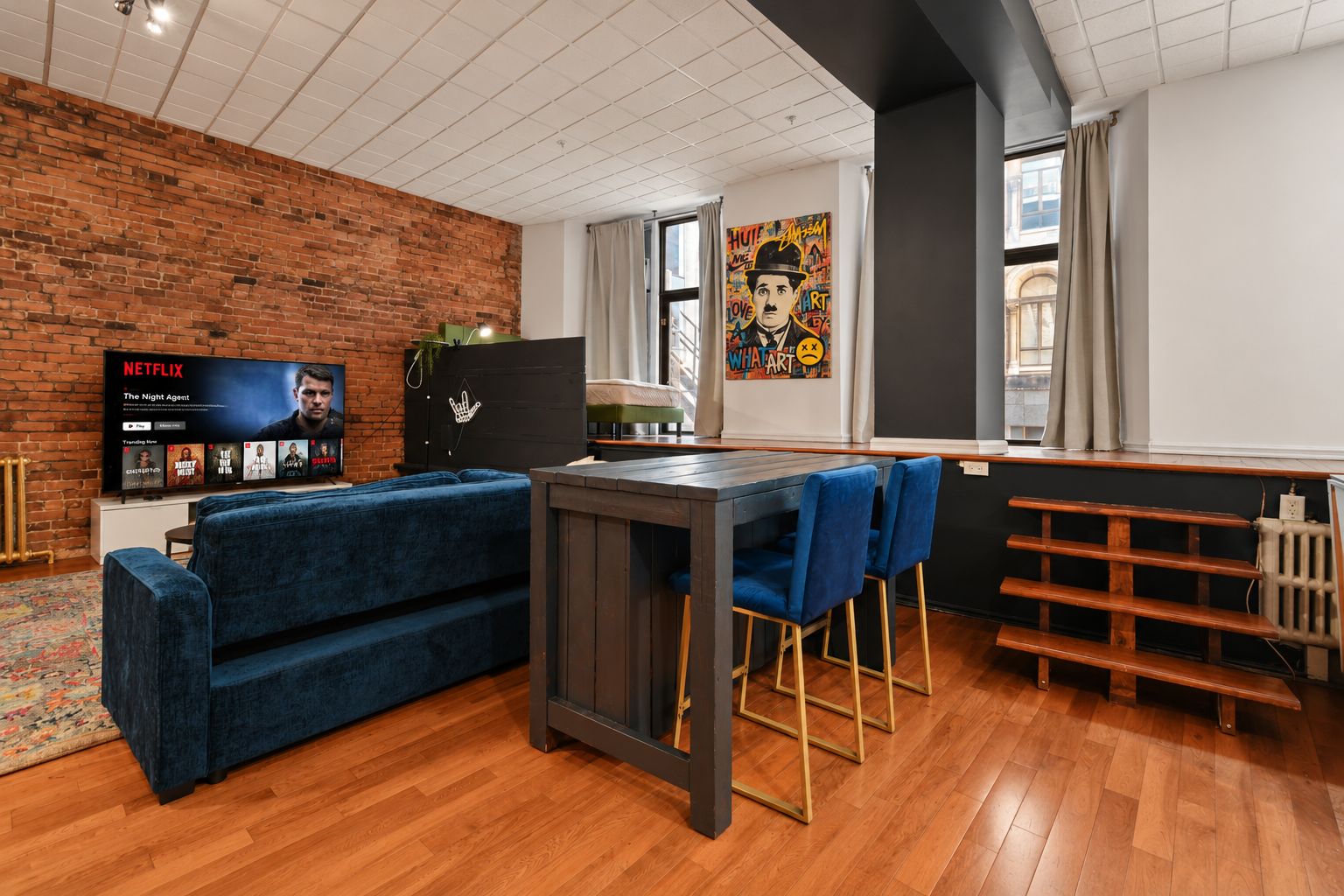 Un salon moderne avec un mur en briques, un téléviseur à écran plat, un canapé bleu et un coin bar avec des tabourets.