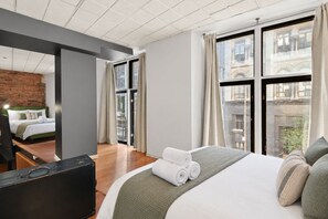 Ein modernes Hotelzimmer mit einem großen Bett, einem Schreibtisch und Blick auf eine Stadtlandschaft durch große Fenster.
