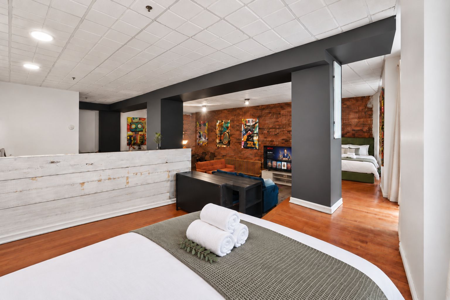 A hotel room with a large bed, a seating area, a reception desk, and a brick wall.