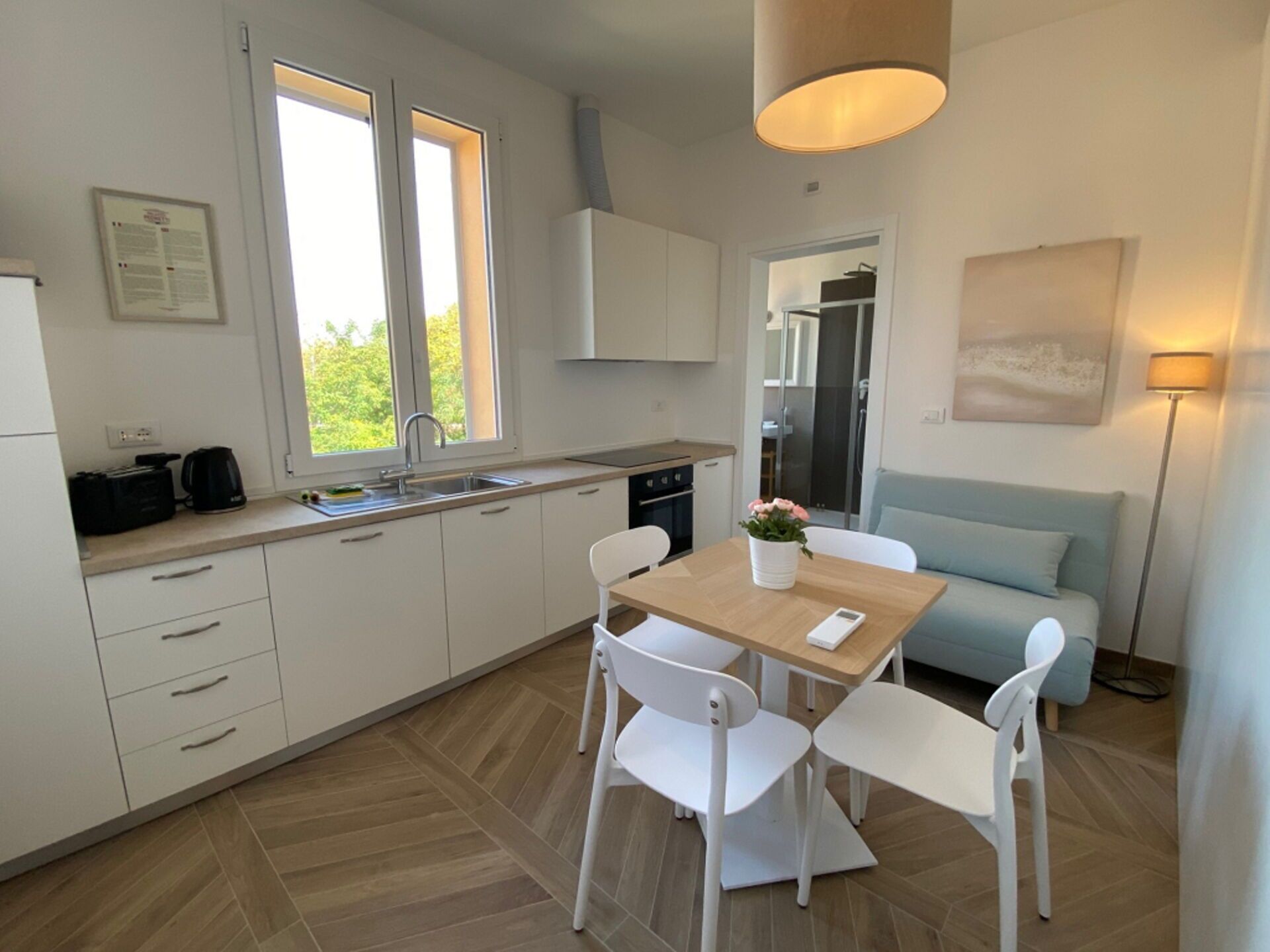 A modern kitchen with white cabinets, a dining table with chairs, a coffee maker, and a window.