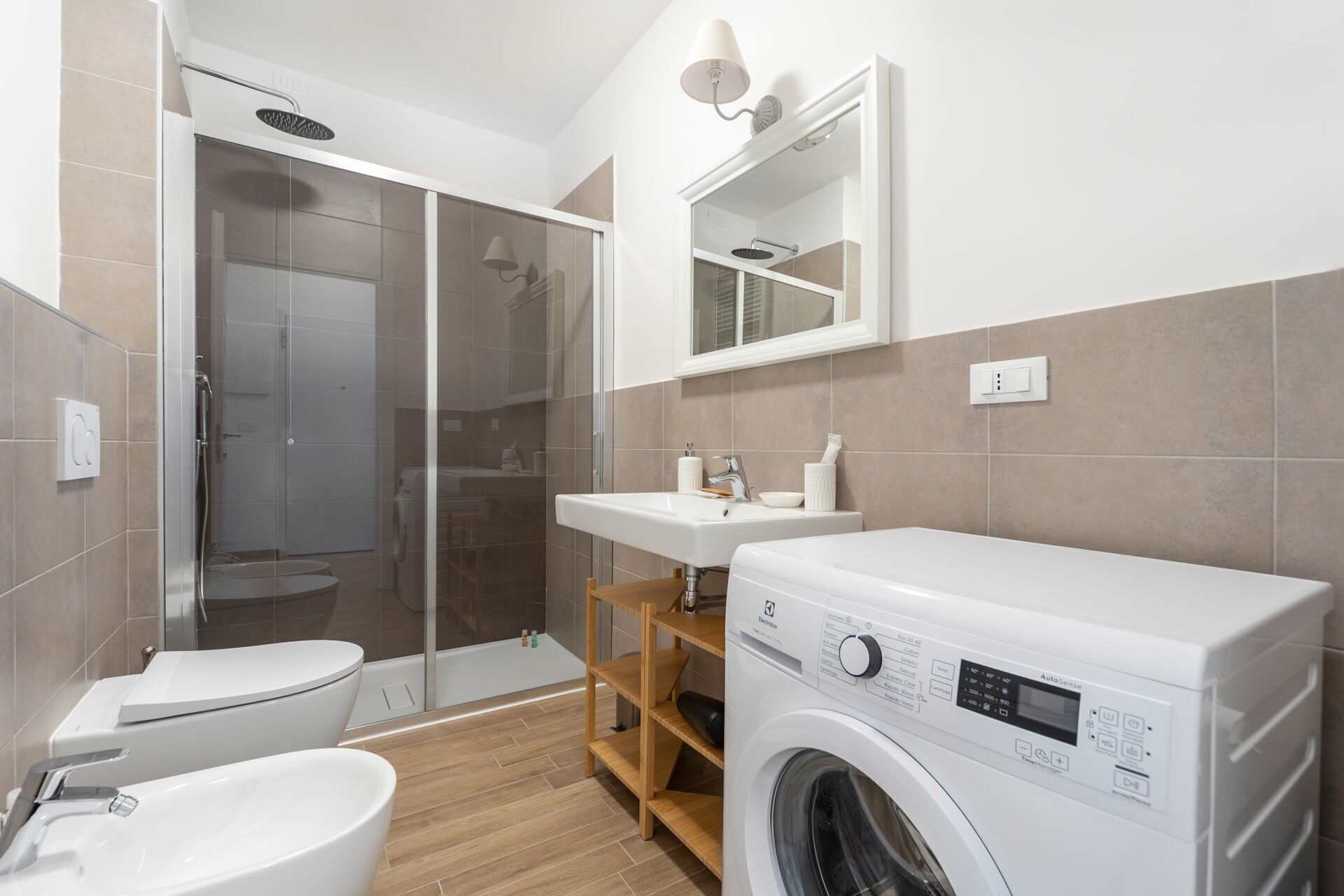 Een moderne badkamer met een douchecabine van glas, een toilet, een wastafel en een voorlader wasmachine.