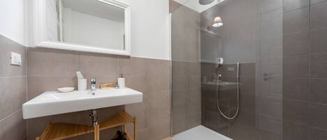Un baño moderno con lavamanos, espejo y ducha blancos.