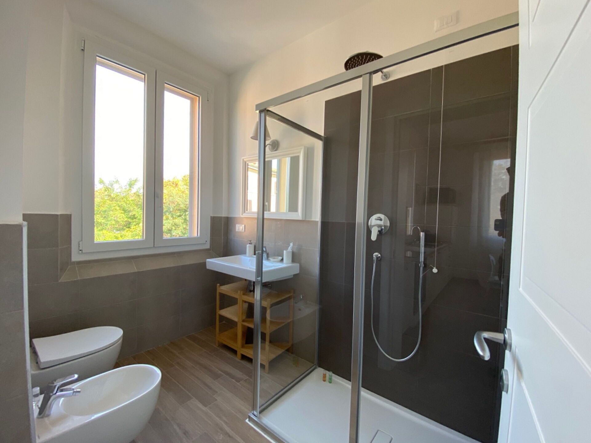 A modern bathroom with a glass-enclosed shower, a standalone bathtub, and a window providing natural light.
