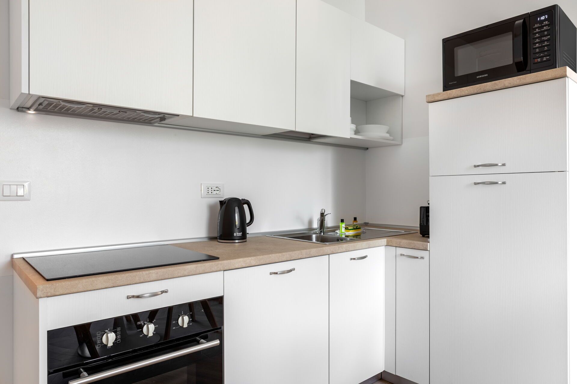 A modern kitchen with white cabinets, a built-in oven, a microwave, and a coffee maker.