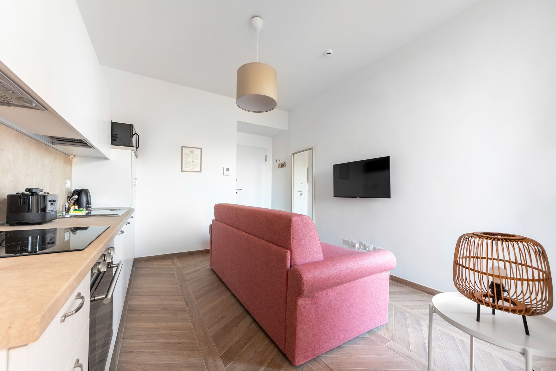 A modern kitchen with a red sofa, a TV mounted on the wall, and a wicker chair.