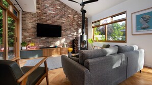 Un salon moderne avec un mur en briques, une cheminée, un canapé, un téléviseur et une grande fenêtre donnant sur des arbres.