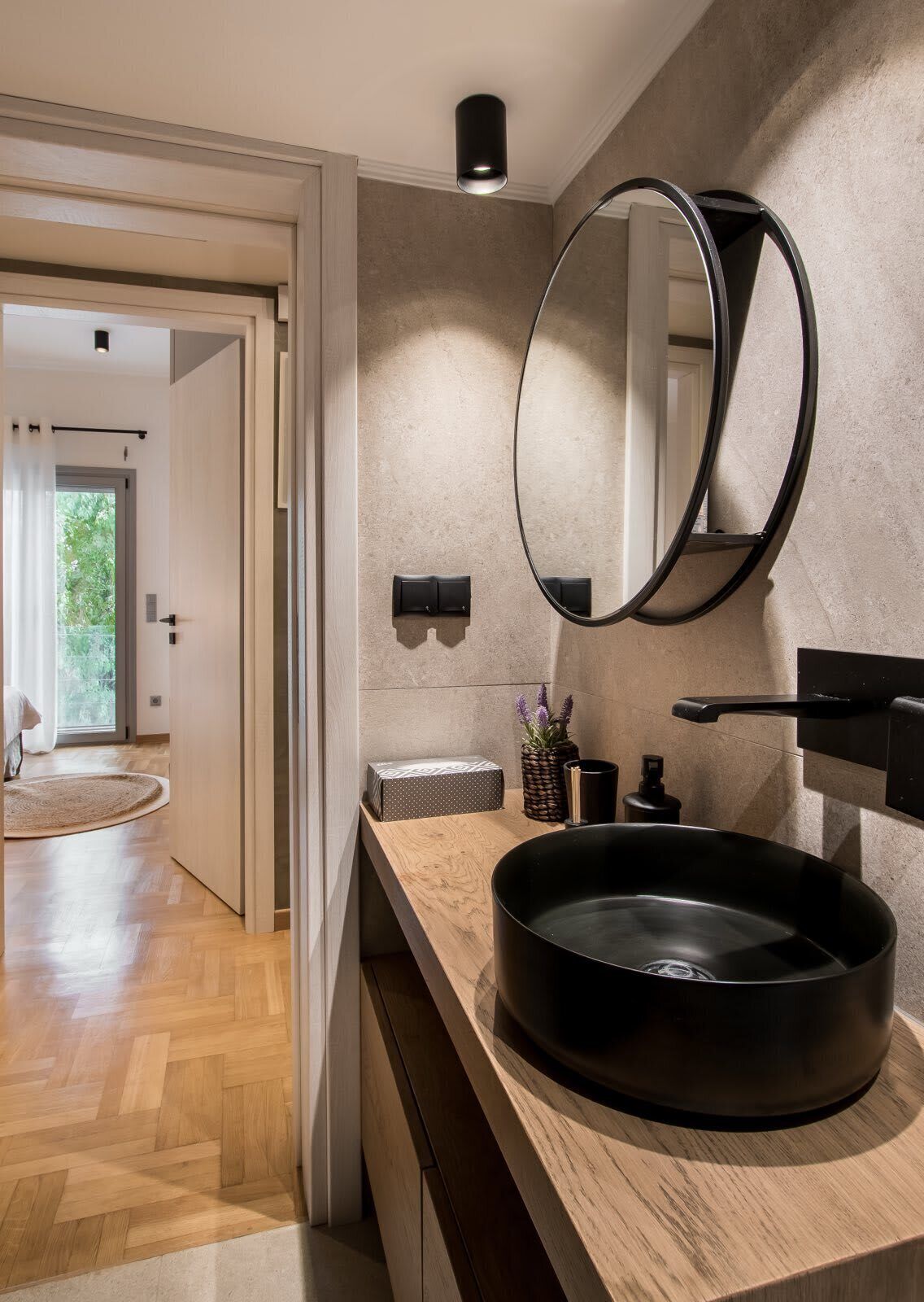 Un baño moderno con un lavamanos redondo negro, un espejo grande y un mueble de tocador de madera.